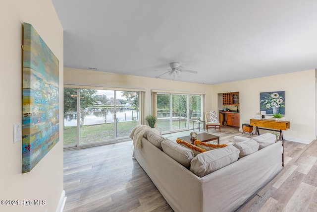 living room featuring ceiling fan, a water view, and light wood-type flooring