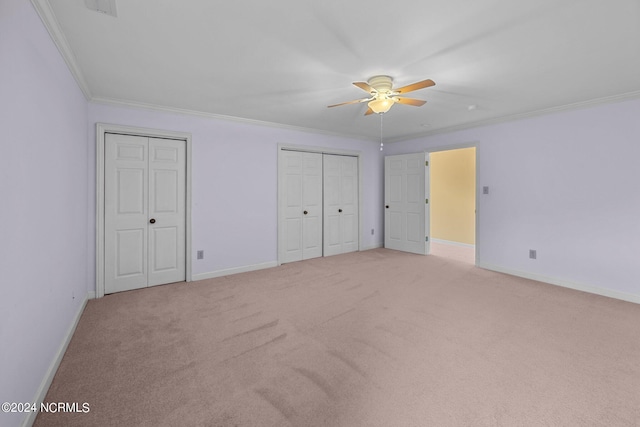 unfurnished bedroom featuring ceiling fan, ornamental molding, light colored carpet, and two closets