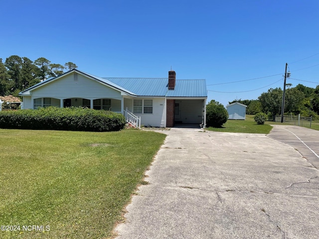 ranch-style home with a chimney, a front yard, metal roof, an attached carport, and driveway