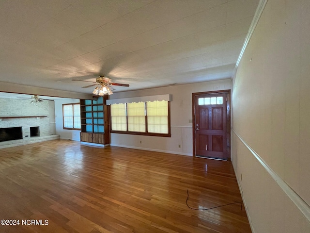 unfurnished living room with ceiling fan, ornamental molding, a fireplace, and wood finished floors