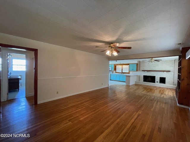 unfurnished living room featuring ceiling fan, a fireplace, baseboards, and wood finished floors