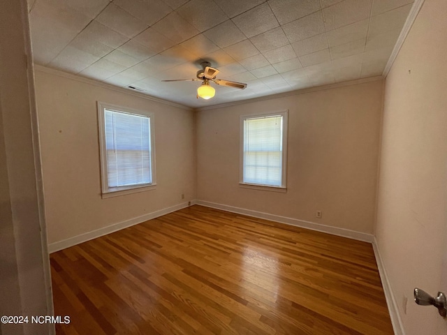 spare room featuring wood finished floors, visible vents, a ceiling fan, baseboards, and ornamental molding