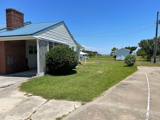 view of property exterior featuring brick siding, a chimney, concrete driveway, a lawn, and metal roof