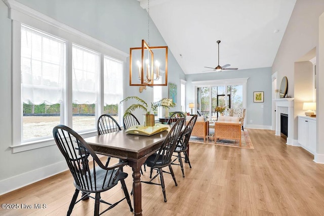 dining room with ceiling fan with notable chandelier, high vaulted ceiling, and light wood-type flooring