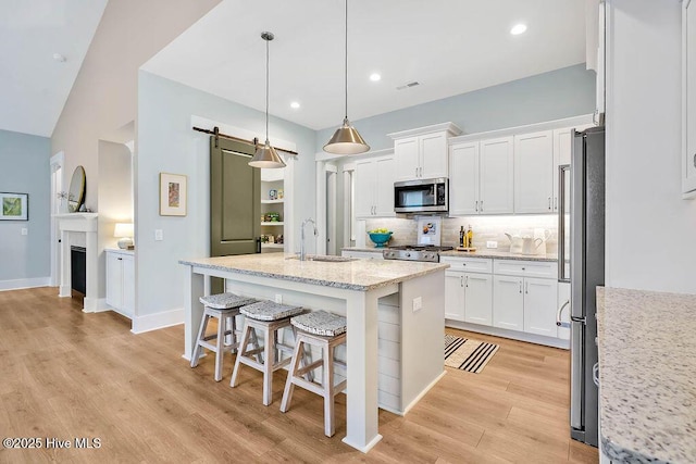 kitchen with stainless steel appliances, a barn door, an island with sink, and white cabinets