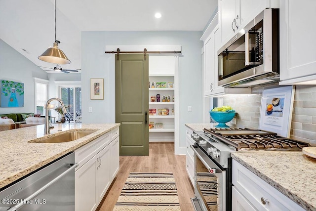 kitchen with appliances with stainless steel finishes, white cabinetry, sink, hanging light fixtures, and light stone countertops