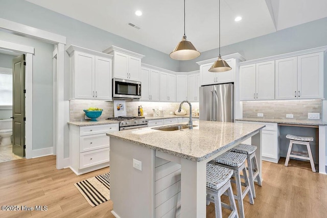 kitchen with sink, white cabinetry, light stone counters, an island with sink, and stainless steel appliances