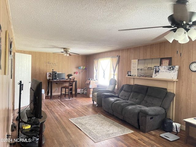 living room with hardwood / wood-style flooring, ceiling fan, wooden walls, and a textured ceiling