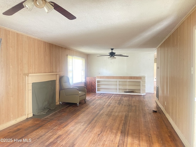 unfurnished living room with ceiling fan, wooden walls, dark hardwood / wood-style flooring, and a textured ceiling