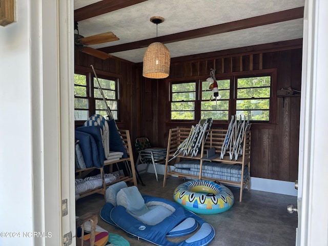 misc room with beamed ceiling, ceiling fan, and wood walls