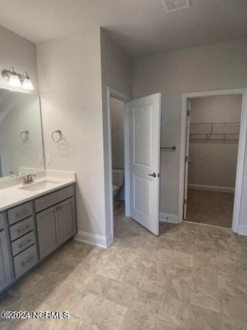 bathroom with a walk in closet, visible vents, toilet, baseboards, and vanity