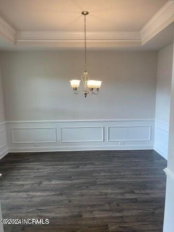 unfurnished dining area with a tray ceiling, dark wood-style floors, crown molding, and a chandelier