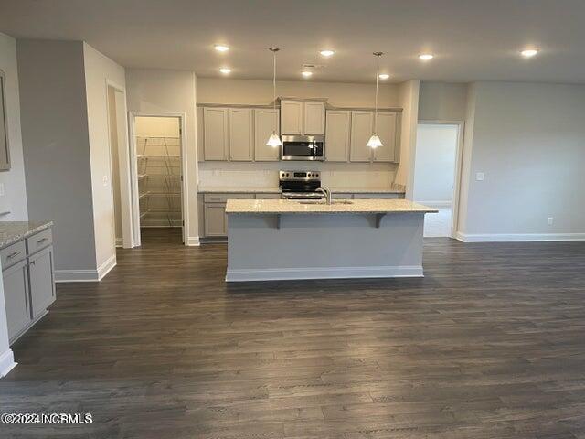 kitchen with appliances with stainless steel finishes, a breakfast bar area, dark wood-type flooring, and a kitchen island with sink