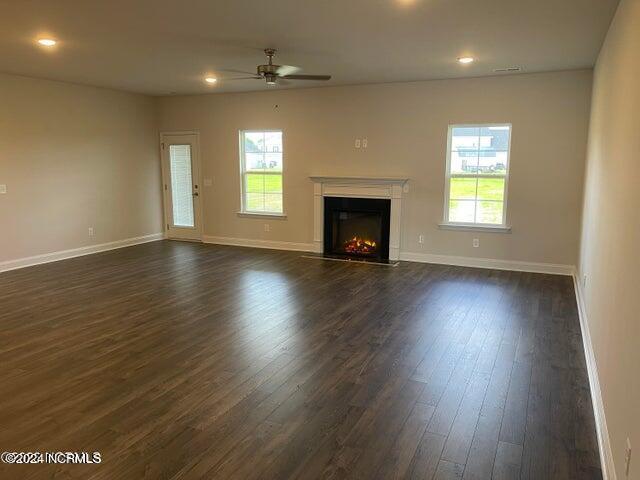 unfurnished living room with baseboards, plenty of natural light, a glass covered fireplace, and dark wood-style flooring