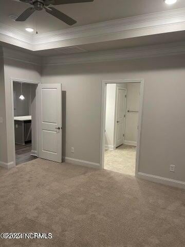 unfurnished bedroom featuring connected bathroom, baseboards, ornamental molding, light carpet, and a raised ceiling