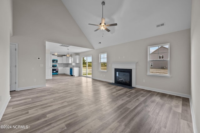 unfurnished living room with ceiling fan, light wood-type flooring, and high vaulted ceiling