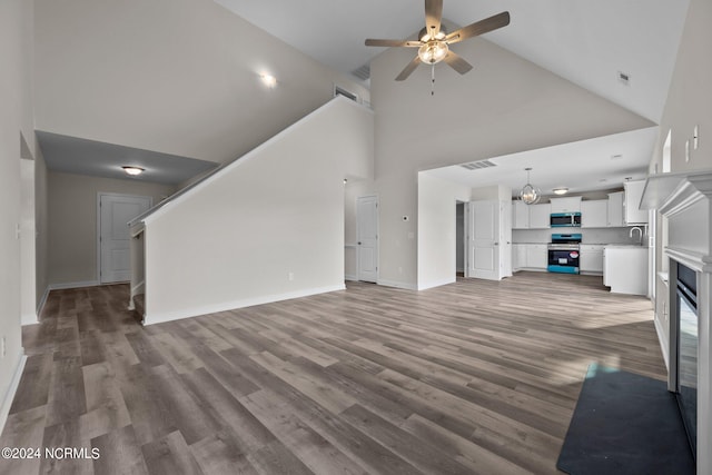 unfurnished living room featuring hardwood / wood-style flooring, ceiling fan with notable chandelier, sink, and high vaulted ceiling