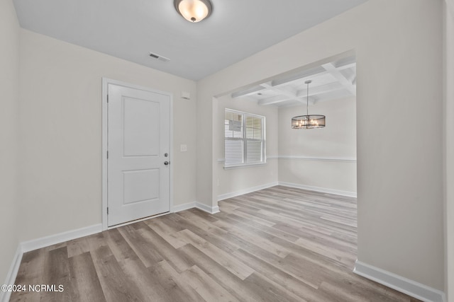 empty room with a notable chandelier, light wood-type flooring, beam ceiling, and coffered ceiling