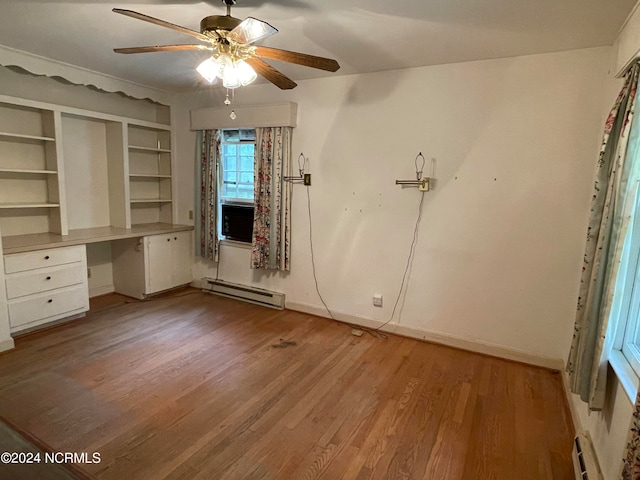 empty room featuring built in desk, ceiling fan, hardwood / wood-style flooring, and baseboard heating