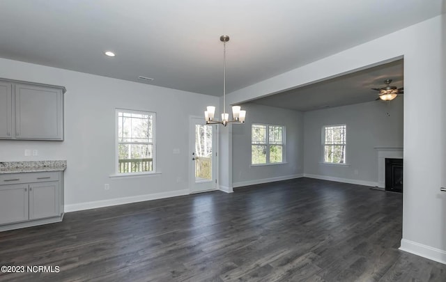 unfurnished dining area with ceiling fan with notable chandelier, dark wood-type flooring, and a healthy amount of sunlight