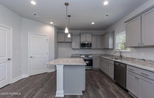 kitchen featuring sink, light stone counters, a center island, hanging light fixtures, and appliances with stainless steel finishes