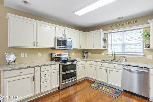 kitchen featuring appliances with stainless steel finishes, dark wood-type flooring, light stone countertops, white cabinetry, and a sink