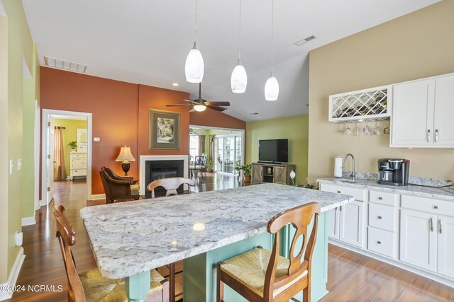 kitchen with light stone counters, a fireplace, visible vents, white cabinets, and a kitchen bar