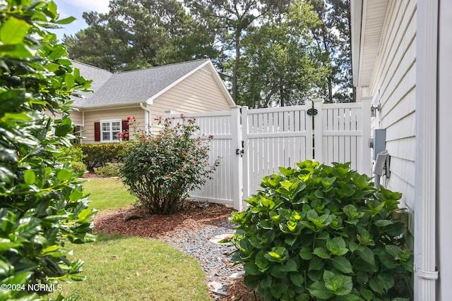 view of side of property featuring roof with shingles, fence, and a gate