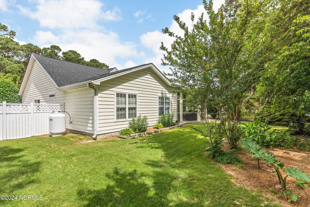 rear view of house featuring roof with shingles, a lawn, and fence