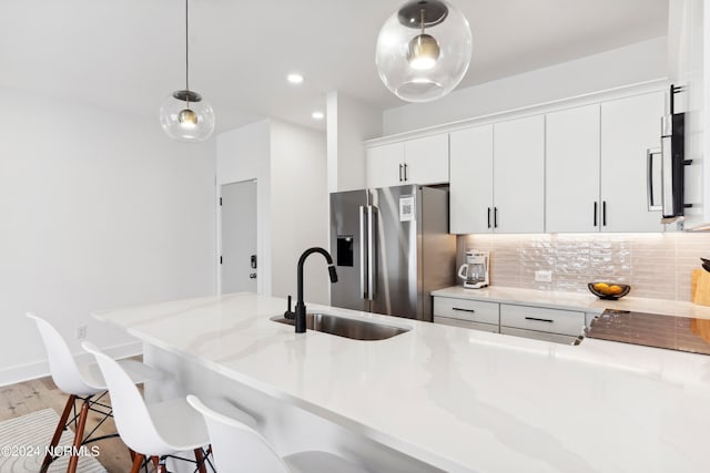 kitchen featuring a kitchen bar, high quality fridge, sink, pendant lighting, and white cabinets