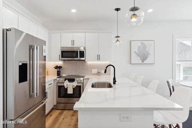 kitchen with hanging light fixtures, white cabinetry, sink, and stainless steel appliances