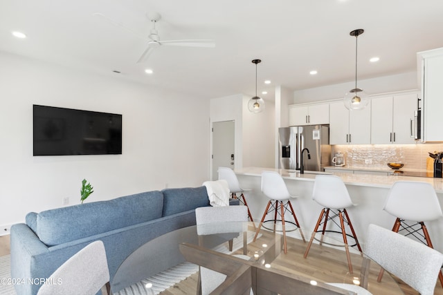 living room featuring ceiling fan, sink, and light wood-type flooring