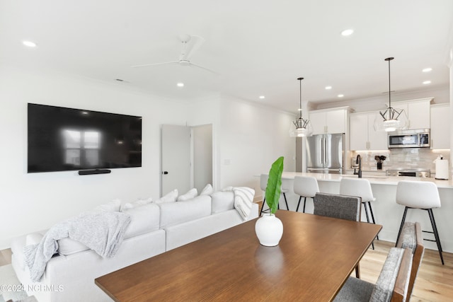 dining area featuring light hardwood / wood-style flooring, ceiling fan, crown molding, and sink