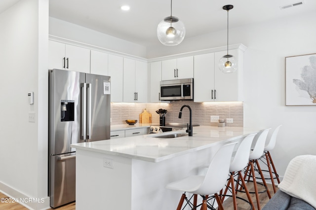 kitchen with kitchen peninsula, appliances with stainless steel finishes, sink, pendant lighting, and white cabinetry