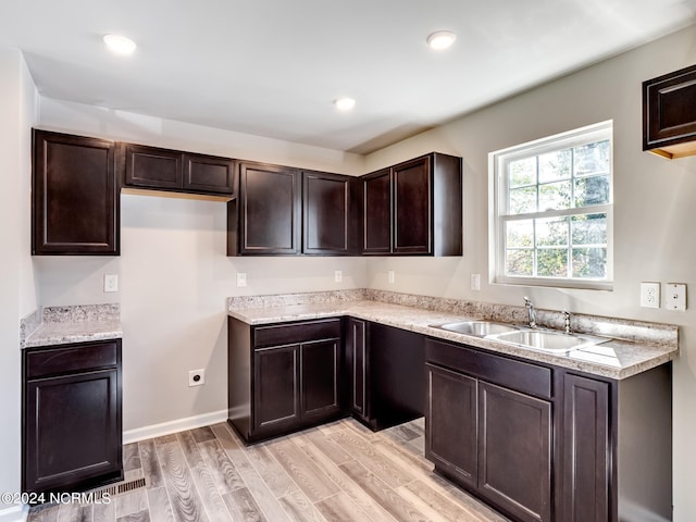 kitchen featuring light hardwood / wood-style flooring, dark brown cabinets, sink, and light stone countertops