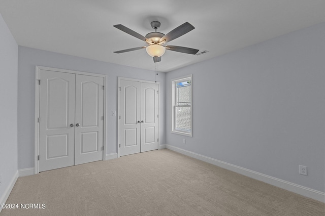 unfurnished bedroom featuring multiple closets, light carpet, and ceiling fan