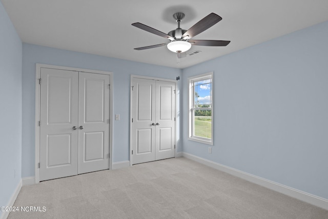 unfurnished bedroom with light carpet, ceiling fan, and two closets