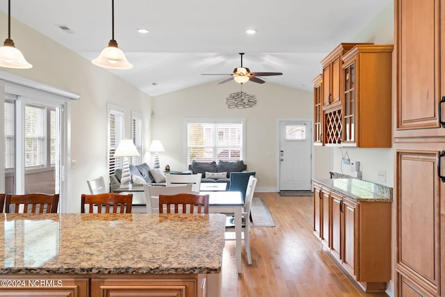 kitchen featuring hanging light fixtures, light hardwood / wood-style flooring, vaulted ceiling, and light stone countertops