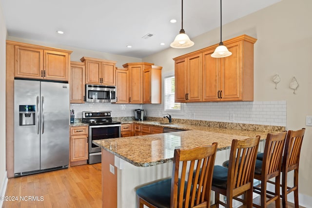 kitchen featuring appliances with stainless steel finishes, a kitchen bar, tasteful backsplash, light hardwood / wood-style flooring, and pendant lighting