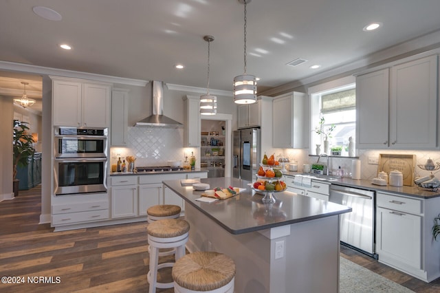 kitchen with appliances with stainless steel finishes, a center island, wall chimney exhaust hood, tasteful backsplash, and dark wood-type flooring