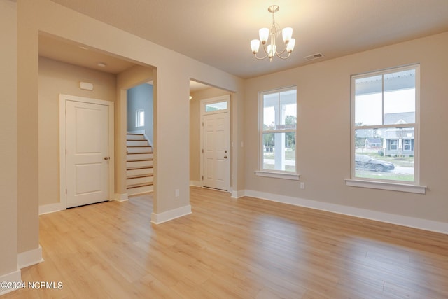 spare room with plenty of natural light, light wood-type flooring, and a chandelier