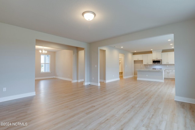 unfurnished living room with a notable chandelier and light wood-type flooring