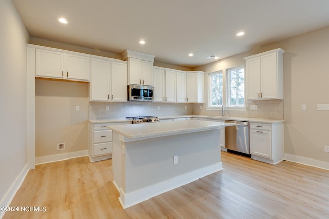 kitchen featuring appliances with stainless steel finishes, a kitchen island, white cabinets, light hardwood / wood-style floors, and backsplash