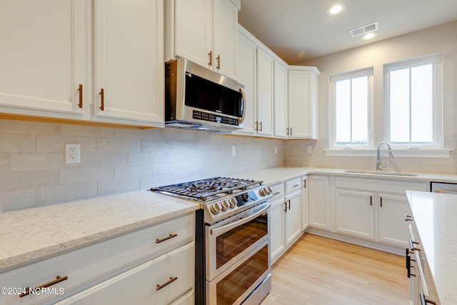 kitchen featuring backsplash, appliances with stainless steel finishes, sink, and light wood-type flooring