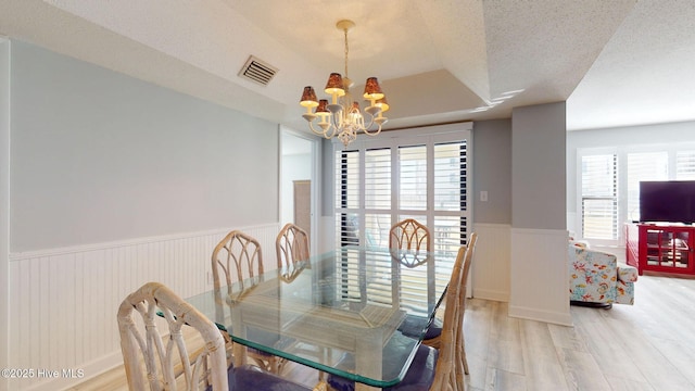 dining area with a raised ceiling, a wealth of natural light, a chandelier, and a textured ceiling