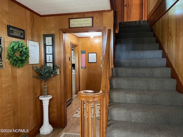 stairway featuring a baseboard radiator, hardwood / wood-style floors, wooden walls, and ornamental molding