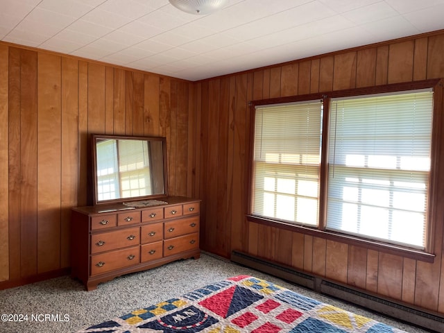 unfurnished bedroom with light colored carpet, wood walls, and baseboard heating