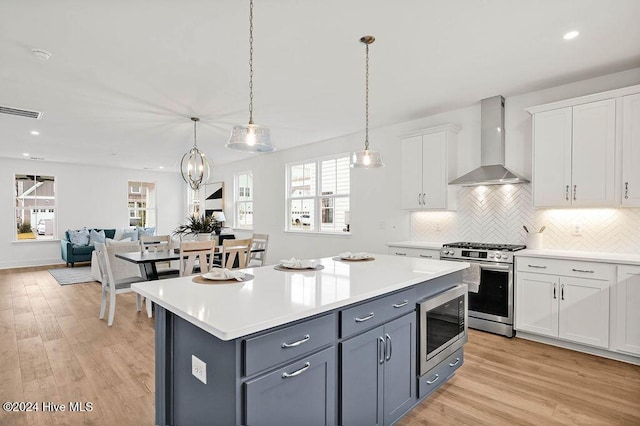 1134 Trisail Ter, Wilmington, NC 28412 - kitchen featuring wall chimney range hood, stainless steel appliances, white cabinetry, light countertops, and light wood finished floors