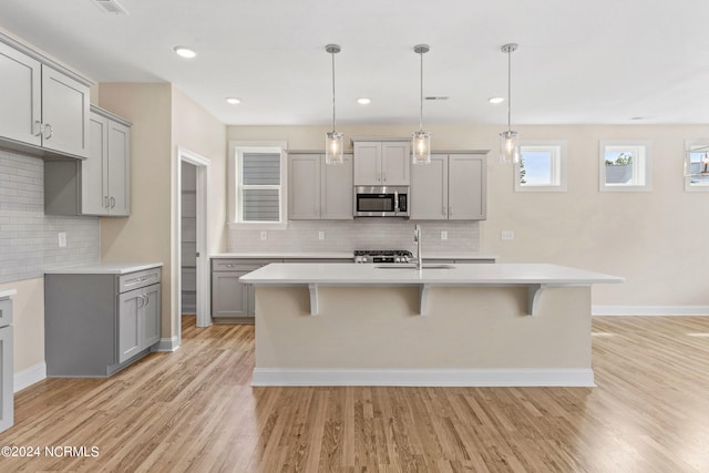 kitchen featuring stainless steel microwave, light wood-style flooring, gray cabinets, and light countertops