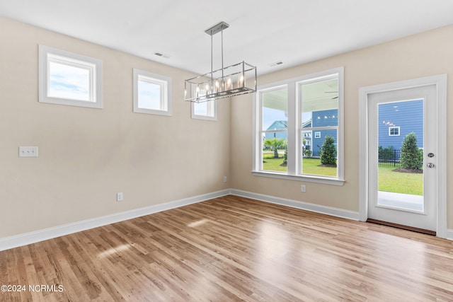 unfurnished dining area featuring an inviting chandelier, wood finished floors, baseboards, and visible vents